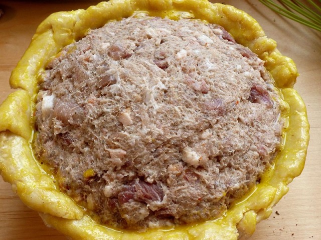 The pie filled with forcemeat and eggs, the edges of the pastry brushed with beaten egg